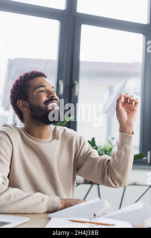 Smiling african american businessman holding paper plane in office Stock Photo