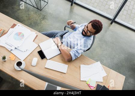 Overhead view of african american businessman looking at computer monitor near papers on table Stock Photo
