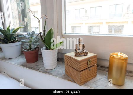 Zen golden Buddha statue sitting meditating near the window with plants. candlelight and chest in the background. Stock Photo