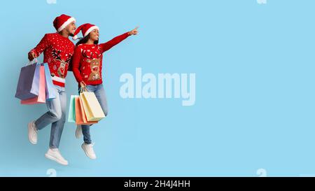 Excited african american lovers in Santa hats holding shopping bags Stock Photo