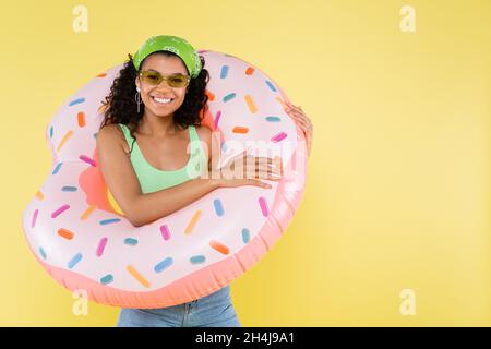 positive african american young woman standing with inflatable ring isolated on yellow Stock Photo
