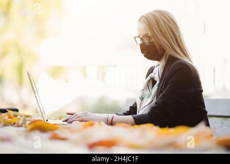 Young businesswoman with covid face mask working on laptop outside Stock Photo