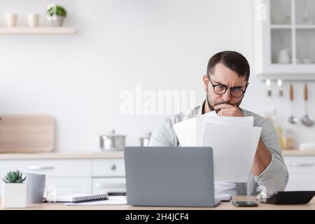 Sad busy mature caucasian businessman in glasses working with documents and laptop Stock Photo