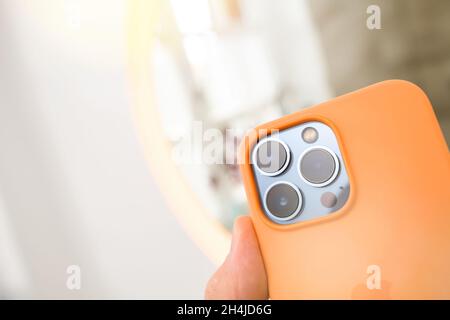 Close-up POV male hand holding latest Apple Computers iPhone 13 pro with orange silicone protection case and all three rear cameras Stock Photo