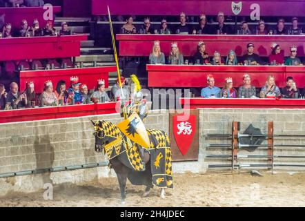 Medieval Castle Restaurant and Tournament: Knight wearing armor sits on horse that wears black-and-yellow checkered attire, with the knight holding a Stock Photo