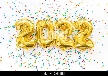 Happy New year 2022 celebration. Gold and silver foil balloons numeral 2022 and confetti on pink background. Christmas Flat lay Stock Photo