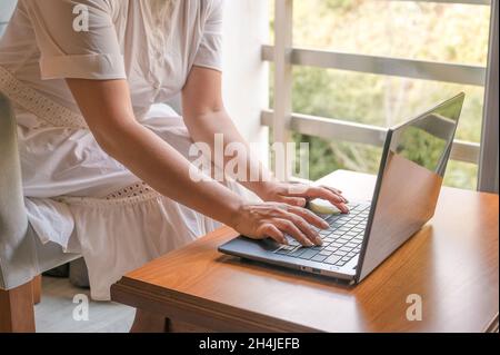 freelancer working with laptop at home by the window, education and remote work, programmer, online business. hands of an adult woman laptop keyboard. Stock Photo