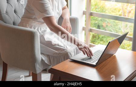 Woman hands using computer laptop at home interior. unrecognizable woman is sitting by the window in the living room and working on a laptop Stock Photo