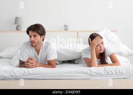 Offended angry young caucasian couple lying on bed ignoring partner in bedroom Stock Photo