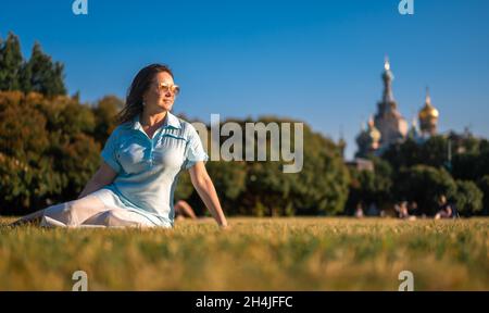 Woman in autumnal park. lonely middle-aged woman sitting on grass and looking away happy. Middle aged caucasian woman sits alone at golden autumn park Stock Photo