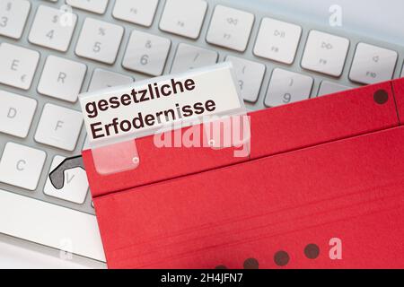 The German words for legal requirements can be seen on the label of a red hanging folder. The hanging folder is on a computer keyboard. Stock Photo