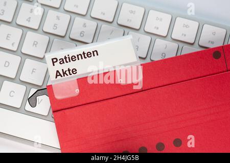 The German word for Patient file can be seen on the label of a red hanging folder. The hanging folder is on a computer keyboard. Stock Photo