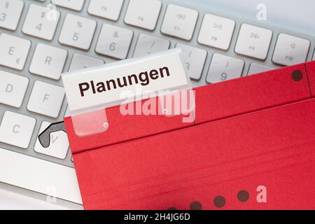 The German word for Planning can be seen on the label of a red hanging folder. The hanging folder is on a computer keyboard. Stock Photo