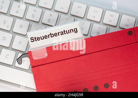 The German word for Tax advice can be seen on the label of a red hanging folder. The hanging folder is on a computer keyboard. Stock Photo