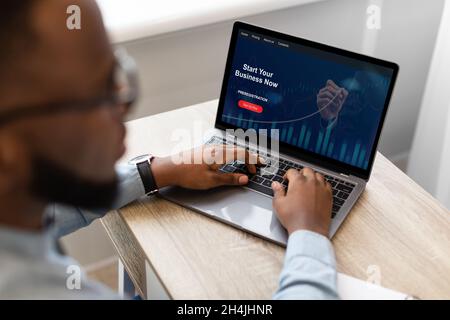 Millennial black businessman work at laptop with graph on screen, checks financial profit in office Stock Photo