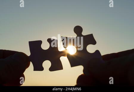 Puzzle pieces are connected. Puzzle pieces in hand on a sunny sky background. Business, partner, solution, alliance, union concept. High quality photo Stock Photo