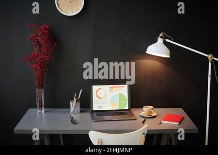 Image of computer with financial report on the screen on the table with modern black wall in front of it Stock Photo