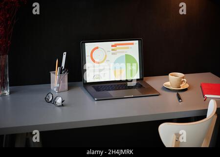 Image of laptop with statistics graphs on laptop screen on the table at modern office Stock Photo
