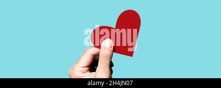 a young man gives a red heart on a blue background, in a panoramic format to use as web banner or header Stock Photo