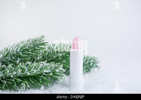 A white tube of pink lipstick balm to protect and nourish lips. Winter season cosmetics. Mock up container near with snowflakes, in the snow. Christma Stock Photo