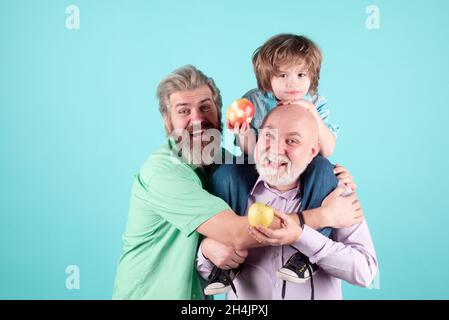 Grandfather father and on hugging and eating apple. Men in different ages with tenderness hug, child love, affectionate. Stock Photo