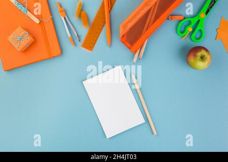 Blank paper with pen, school or office workspace with orange supplies on blue background. Flat lay. Stock Photo