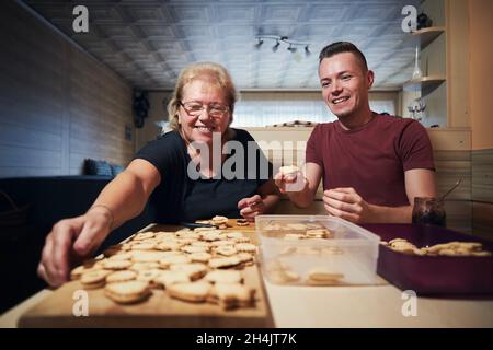 Young adult man helping his mom with baking Christmas sweets at home kitchen. Tradition during advent in Czech Republic. Stock Photo