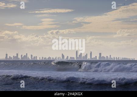 Unidentified surfer catching waves off Coolangatta Beach with the Gold Coast in the background Stock Photo