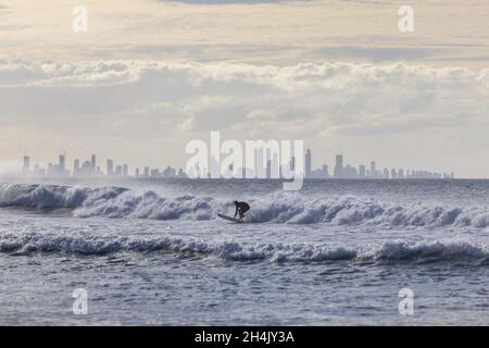 Unidentified surfer catching waves off Coolangatta Beach with the Gold Coast in the background Stock Photo