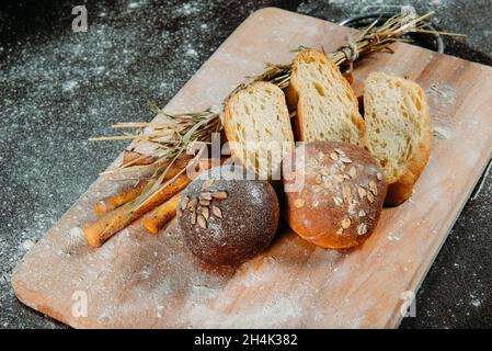 Assorted bread rolls, slices of bread and breadsticks on a chopping board Stock Photo