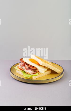 Breakfast sandwich with egg, bacon and vegetables on grey close-up Stock Photo