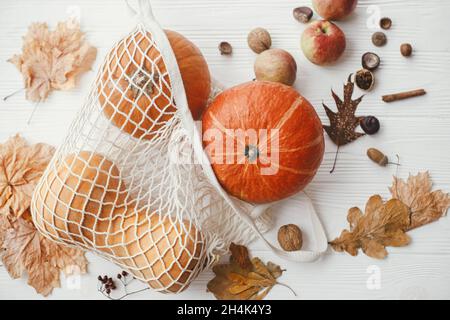 Pumpkins in string bag, apples, nuts and autumn leaves on white wooden background. Autumnal Flat lay. Zero waste concept, plastic free shopping. Harve Stock Photo
