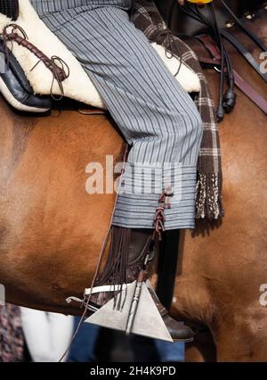 Close-up of a rider's leg in the stirrup of a horse dressed in cowboy clothing Stock Photo