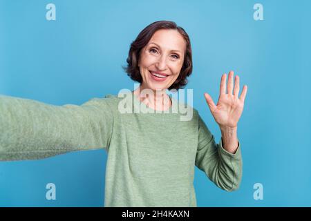 Photo of aged grey hair woman do selfie wave hand wear green jumper isolated on blue color background Stock Photo