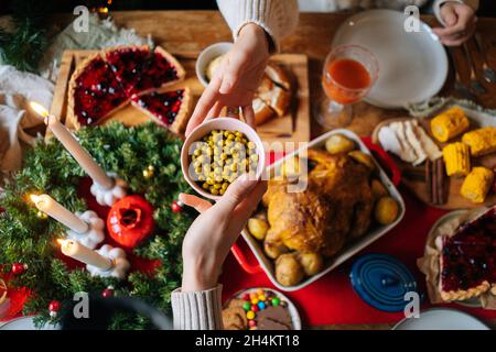 Close-up top view of unrecognizable young woman and man passing delicious food sitting at festive Christmas table during holiday family frindly party. Stock Photo