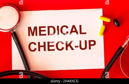 On a white sheet and a red background the inscription MEDICAL CONTROL, next to a stethoscope and pills. Concept of medicine and health care. Stock Photo