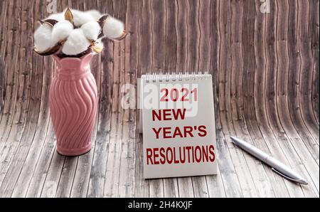 text of RESOLUTION NEW YEAR 2021, on notepad and wooden table. There is a bouquet of cotton in a vase on the table Stock Photo