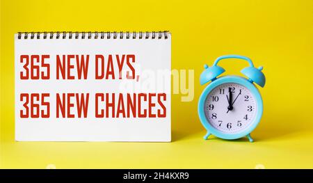 365 new days, 365 new chances: the quote is written on a notebook and on a yellow paper background, next to an alarm clock Stock Photo