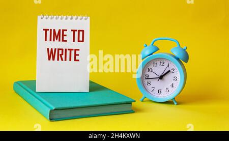 Text for writing words Time to write, text is written on notepad and yellow background. Nearby alarm clock and green notepad. Business concept for urg Stock Photo