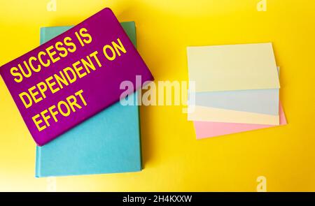 The text Success Depends on Effort is written on a colored notebook that lies on a yellow background Stock Photo