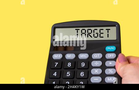 A female hand holds a calculator with the text on the display TARGET on a yellow background, next to colored notepads Stock Photo