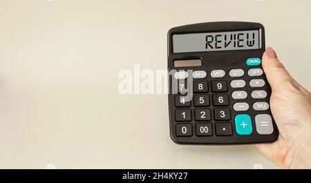 A female hand holds the calculator, the word REVIEW is written on the display. Stock Photo