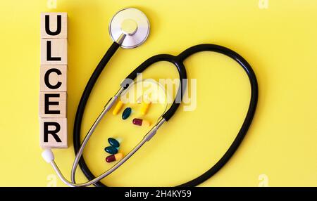 Ulcer inscription on wooden cubes. Section of medicine. A stethoscope and pills lie on a yellow background