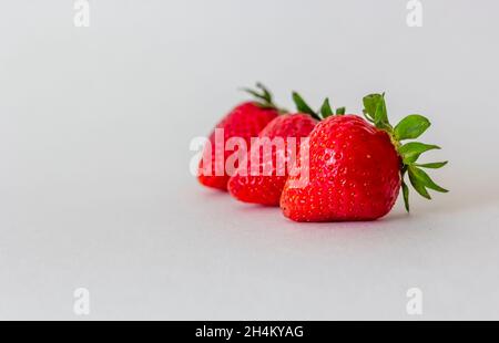 Three strawberries lie on a blue isolated background. There is a place to write Stock Photo