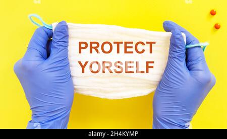 Medical mask with the text protect yourself doctor holds gloves on yellow background Stock Photo