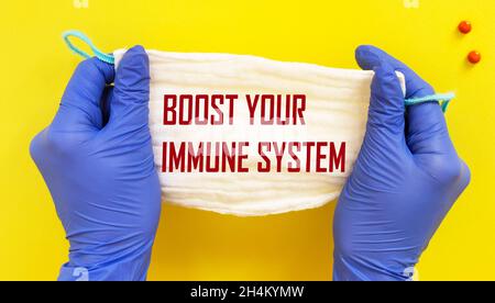 Boost your immune system. Woman in gloves holds a medical mask drawing attention to the phrase, close-up. Composition on yellow background
