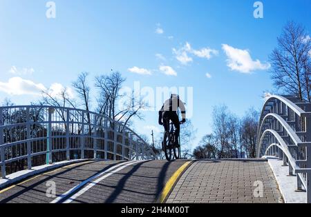 On a sunny spring day, a cyclist rides up a hill, across a bridge on a bicycle path Stock Photo