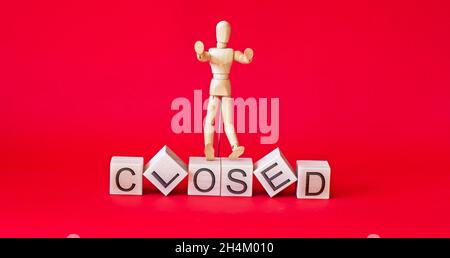 on wooden cubes the text is closed with a wooden doll on a red background Stock Photo