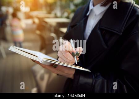 Close-up. Cropped image of unrecognizable young business woman holding a pen and notepad, writing, making notes. Stock Photo