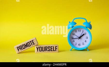 Promote Yourself text written on wooden blocks and yellow background with alarm clock Stock Photo